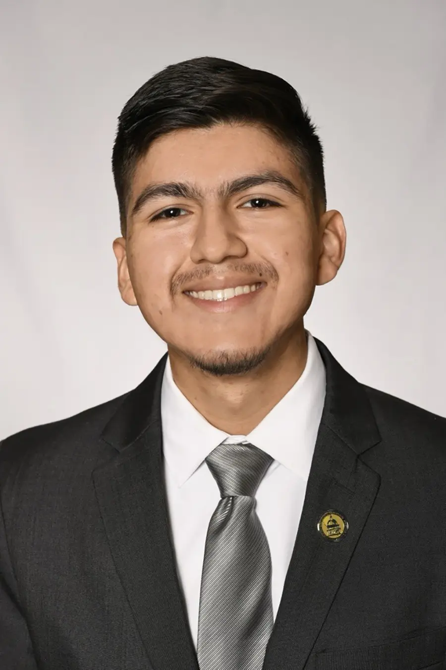 A person in a suit and tie smiling at the camera against a plain background.