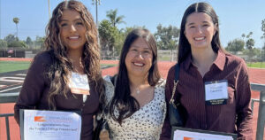 Three smiling students holding scholarship certificates outdoors at Ventura College.