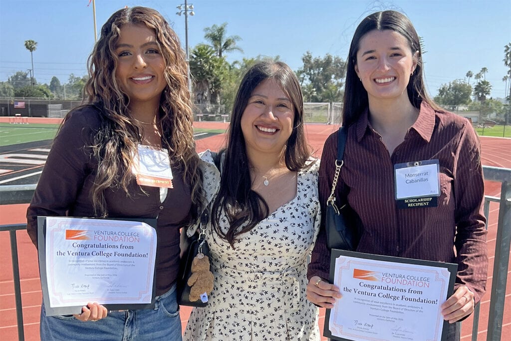 Three smiling women holding scholarship certificates at Ventura College outdoor event.